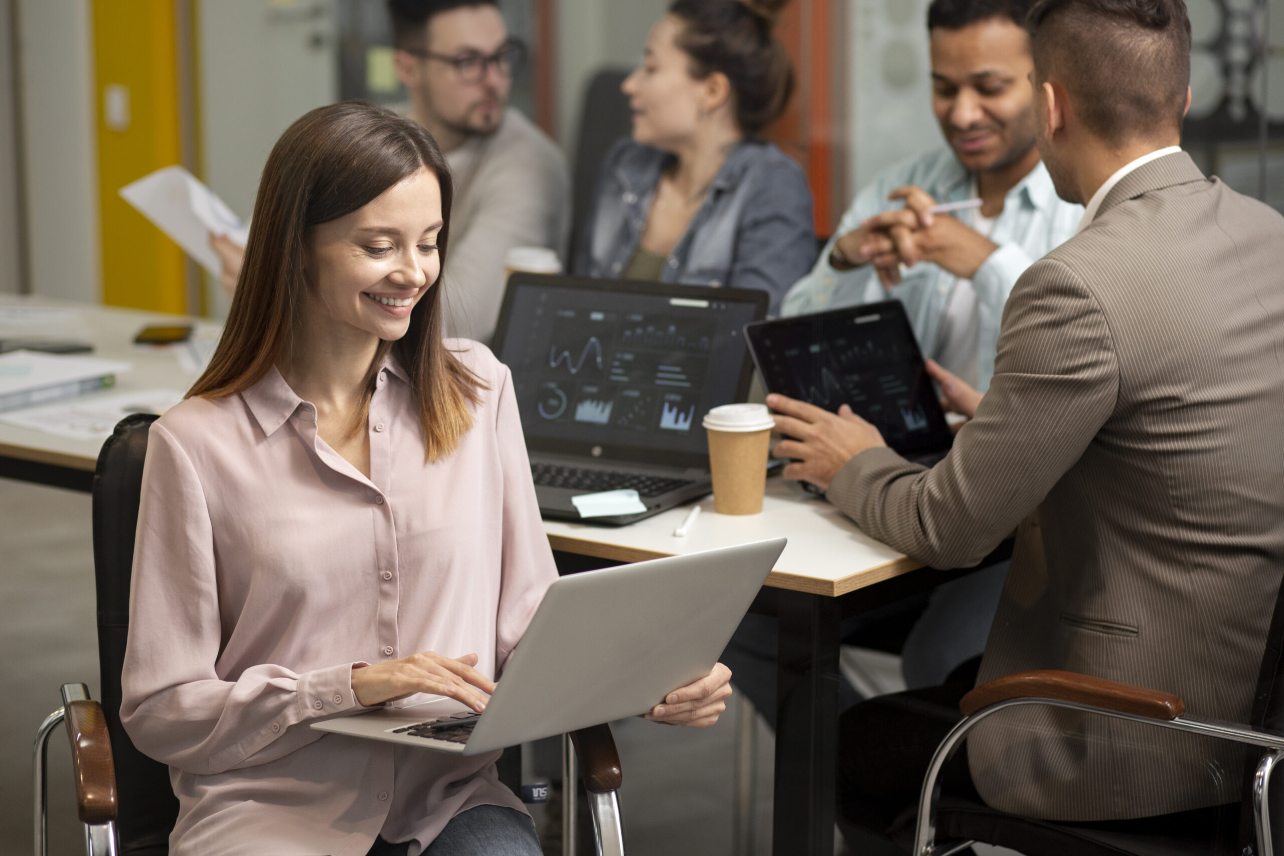 mulher analisando ambiente SAP em seu notebook com seus colegas conversando atrás dela